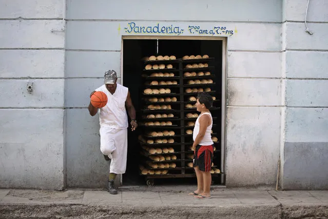 A child looks on as a bakery worker bounces a basketball beside trays of freshly made bread in Havana, Cuba, April 2010. (Photo by Desmond Boylan/Reuters)