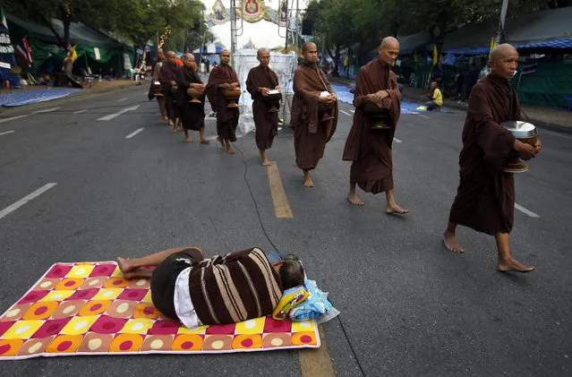 A group of Buddhist monks walk past a sleeping anti-government protester at a protest camp on a road near Government House, where Thai Prime Minister Yingluck Shinawatra's office is located, in Bangkok, Thailand early Wednesday, December 11, 2013. (Photo by Greg Baker/AP Photo)