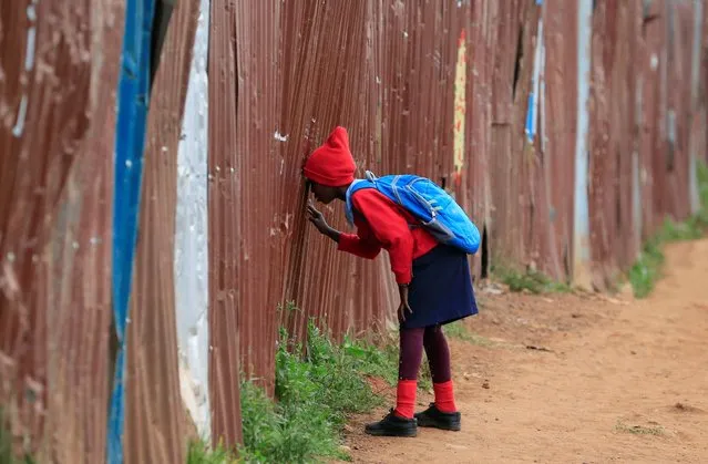 A girl peers through the iron-sheet fence before entering the Stara Rescue Centre and School during the reopening of schools, for the delayed academic year 2021, amid the novel coronavirus disease (COVID-19) pandemic, in Kibera slums of Nairobi, Kenya on July 26, 2021. (Photo by Thomas Mukoya/Reuters)