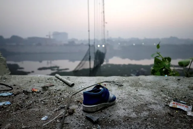 A shoe lies near a damaged suspension bridge after it collapsed on Sunday, in Morbi town in the western state of Gujarat, India on November 1, 2022. Rescue divers were still searching for more bodies in the Machchhu river on November 1, with 134 people confirmed dead – among them 47 children. (Photo by Reuters/Stringer)