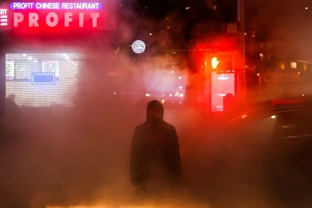A man waits to cross a street during a cold evening as hot steam escapes from the ground in the Manhattan borough of New York on January 16, 2024. New York finally ended a record streak of more than 700 days without measurable snowfall, with a thin layer of white powder covering Central Park and other parts of America's most populous city. (Photo by Charly Triballeau/AFP Photo)