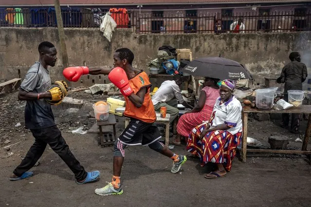 Two amateur boxers practice next to a street stall while promoting an amateur boxing event in the streets of Kampala on January 22, 2024. (Photo by Luis Tato/AFP Photo)