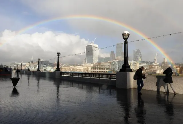 People walk along the Southbank as a rainbow appears over the city of London, on February 4, 2014. (Photo by Nick Ansell/PA Wire)