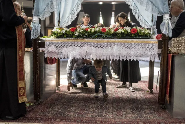 An Orhtodox priest blesses a child passing under a table which symbolizes the grave of Jesus Christ during the Good Friday processions at the main Orthodox church St Kliment in Skopje on April 26, 2019. North Macedonian Orthodox Church celebrates Easter, according to the Julian calendar. (Photo by Robert Atanasovski/AFP Photo)