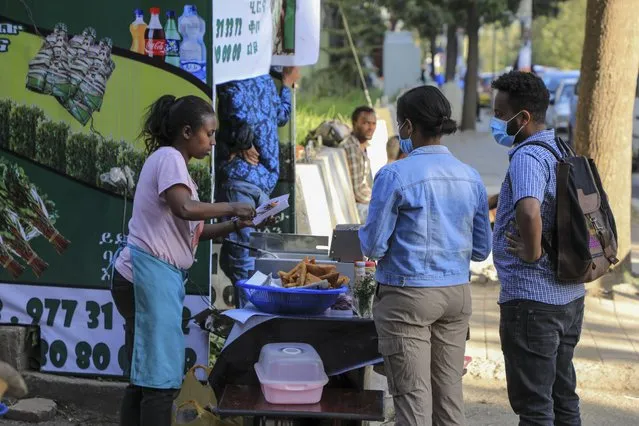Pedestrians buy food from a street vendor in the Piazza old town area of the capital Addis Ababa, Ethiopia Thursday, November 4, 2021. (Photo by AP Photo/Stringer)