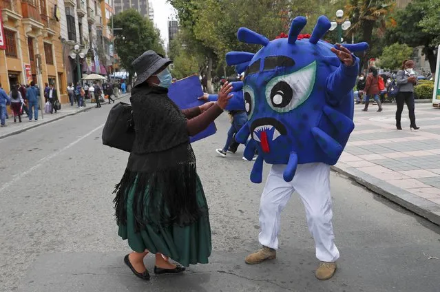 A police officer dressed in a costume representing the COVID-19 virus tries to hug a pedestrian, who resists, along Paseo El Prado as part of an awareness campaign about the spread of the new coronavirus in La Paz, Bolivia, Wednesday, February 10, 2021. (Photo by Juan Karita/AP Photo)