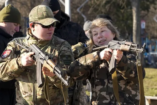 An instructor shows a woman how to use a Kalashnikov assault rifle, as members of a Ukrainian far-right group train, in Kyiv, Ukraine, Sunday, February 13, 2022. Russia denies it intends to invade but has massed well over 100,000 troops near the Ukrainian border and has sent troops to exercises in neighboring Belarus, encircling Ukraine on three sides. U.S. officials say Russia's buildup of firepower has reached the point where it could invade on short notice. (Photo by Efrem Lukatsky/AP Photo)