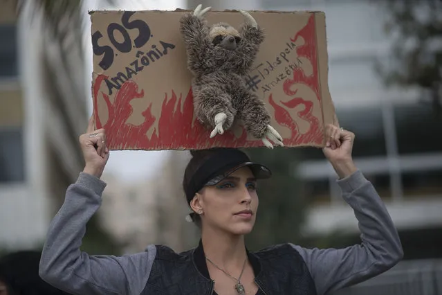 A woman holds up a sign that reads “SOS Amazons. Everybody for the Amazon” featuring a stuffed sloth animal during a protest in defense of the Amazon while wildfires burn in that region, in Rio de Janeiro, Brazil, Sunday, August 25, 2019. Experts from the country's satellite monitoring agency say most of the fires are set by farmers or ranchers clearing existing farmland, but the same monitoring agency has reported a sharp increase in deforestation this year as well. (Photo by Bruna Prado/AP Photo)