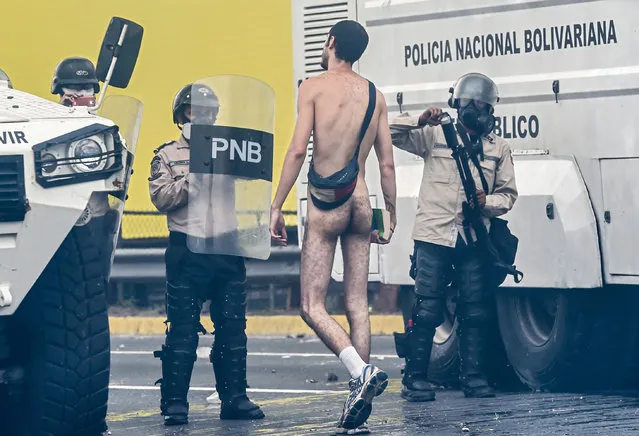 A naked demonstrator remonstrates with riot police during a protest against Venezuelan President Nicolas Maduro, in Caracas on April 20, 2017. Venezuelan riot police fired tear gas Thursday at groups of protesters seeking to oust President Nicolas Maduro, who have vowed new mass marches after a day of deadly unrest. Police in western Caracas broke up scores of opposition protesters trying to join a larger march, though there was no immediate repeat of Wednesday's violent clashes, which left three people dead. (Photo by Juan Barreto/AFP Photo)