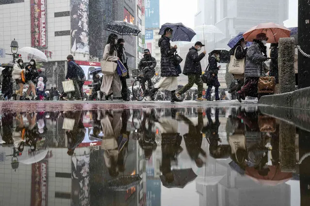 People walk across at the famed Shibuya scramble crossing as the snow comes down Thursday, January 6, 2022, in Tokyo. (Photo by Kiichiro Sato/AP Photo)