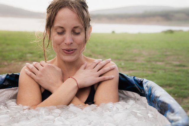 Woman inside a iced bath tube inhaling with eyes closed in the middle of a field. (Photo by Ivan Rodriguez Alba/Getty Images)