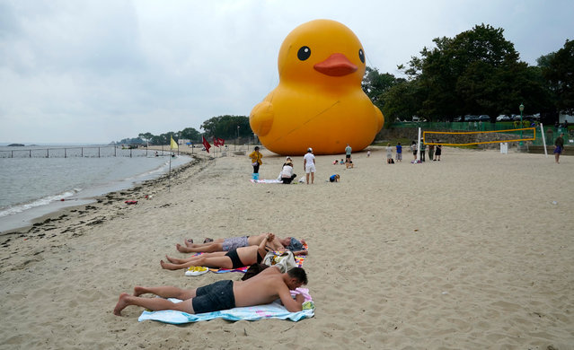 People sunbathe alongside the “World's Largest Rubber Duck” at Rye Playland Beach in Rye, New York, on August 17, 2024. The 61-foot-tall (19-meter) duck, named “Mama Duck”, is spending the weekend at the beach to celebrate the Second Annual Duck Days of Summer. (Photo by Timothy A. Clary/AFP Photo)