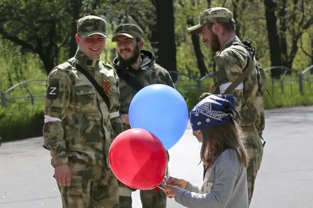 A girl holds balloons as she walks past servicemen of Donetsk People's Republic militia as they patrol a street during celebration of the 77th anniversary of the end of World War II in Mariupol, in territory under the government of the Donetsk People's Republic, eastern Ukraine, Monday, May 9, 2022. (Photo by Alexei Alexandrov/AP Photo)