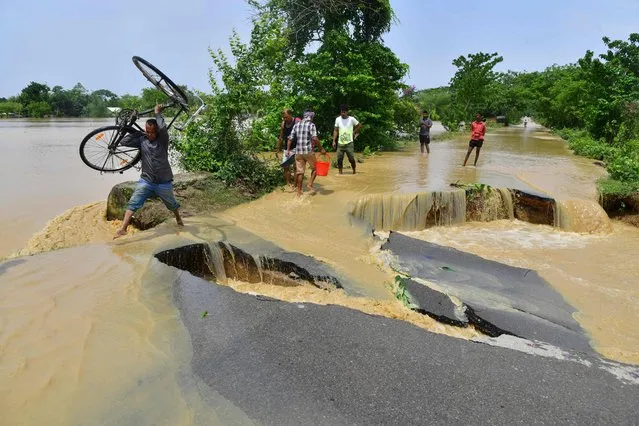 A man carrying his bicycle wades along a partially damaged road due to flooding after unusually heavy rains in Nagaon district, Assam state, on May 19, 2022. (Photo by Biju Boro/AFP Photo)