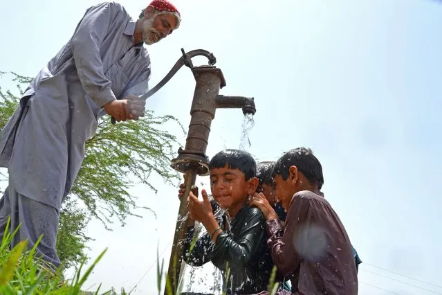A man draws water for the children to cool themselves under a hand pump on a hot summer day in Jaffarabad district of Balochistan on May 9, 2022. (Photo by Fida Hussain/AFP Photo)