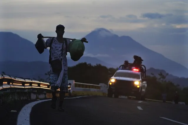 A migrant walks on the highway, followed by a Mexican National Guard vehicle, toward the exit to Huixtla, Chiapas state, Mexico, at sunrise Thursday, June 9, 2022. A group of migrants left Tapachula on Monday, tired of waiting to normalize their status in a region with little work, with the ultimate goal of reaching the U.S. Behind is the Tacana volcano. (Photo by Marco Ugarte/AP Photo)
