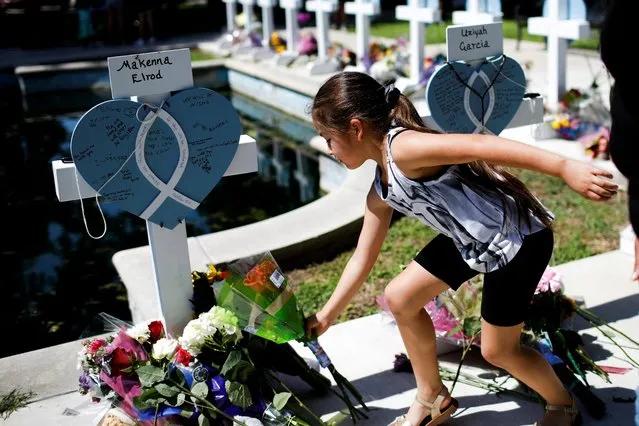 A girl leaves flowers at a memorial in Town Square in front of the county courthouse, two days after a gunman killed nineteen children and two adults, in Uvalde, Texas, U.S. May 26, 2022. (Photo by Marco Bello/Reuters)