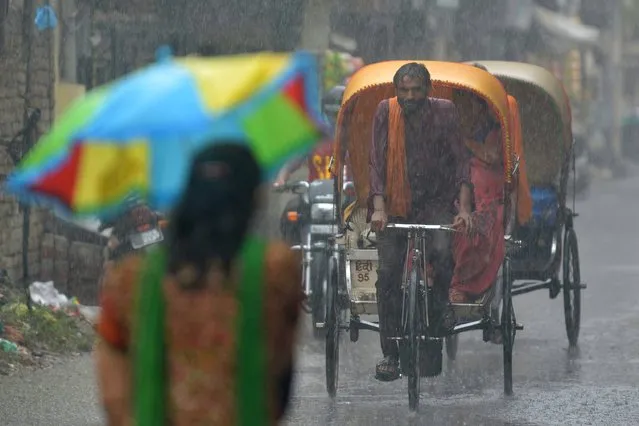 An Indian cycle rickshaw driver transports commuters through a heavy rain downpour in Amritsar on August 1,2017. (Photo by Narinder Nanu/AFP Photo)