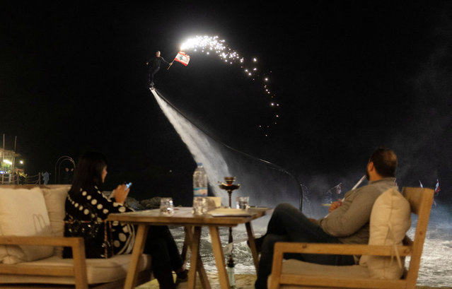 An artist with a Lebanese flag rides a flyboard as he performs for customers at a restaurant, amid the ongoing hostilities between Hezbollah and Israeli forces, in Jounieh, north of Beirut, Lebanon, on November 9, 2024. (Photo by Adnan Abidi/Reuters)