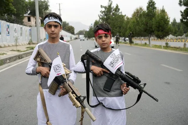 Afghan boys hold eweapons as they pose for a photo during celebrations one year after the Taliban seized the Afghan capital, Kabul, in front of the U.S. Embassy in Kabul, Afghanistan, Monday, August 15, 2022. (Photo by Ebrahim Noroozi/AP Photo)