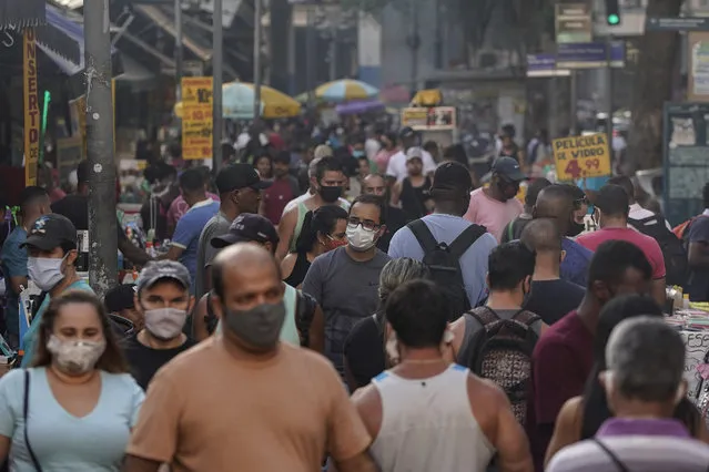 Pedestrians, some wearing protective face masks, walk through a street market in downtown in Rio de Janeiro, Brazil, Thursday, June 25, 2020. Rio continues with its plan to ease restrictive measures due to the new coronavirus and open up the economy to avoid an even worse economic crisis. (Photo by Leo Correa/AP Photo)