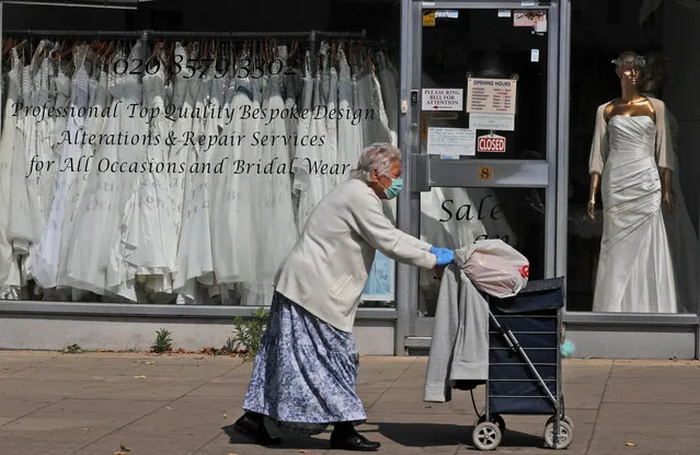 A woman walks past a Wedding dress shop in London, Tuesday, June 9, 2020, where bride dresses pile unused in the shop window. Weddings in the UK have been postponed due to the Covid-19 pandemic and are probably allowed starting in July. (Photo by Frank Augstein/AP Photo)