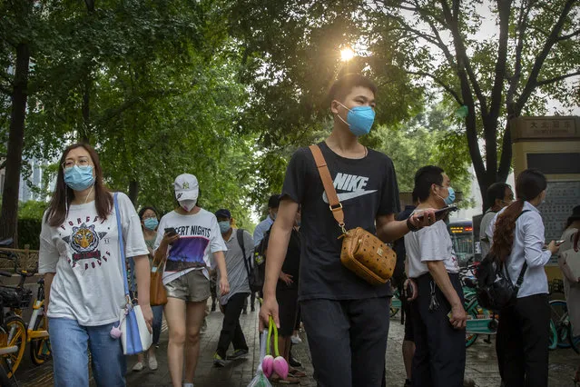 People wearing face masks to protect against the coronavirus walk along a street in Beijing, Friday, July 31, 2020. China is tightening travel restrictions in the capital of Xinjiang, where more than a hundred new cases were reported Friday. (Photo by Mark Schiefelbein/AP Photo)