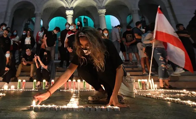 A woman lights candles on the pavement during a candelight vigil for victims of Beirut's blast in front of the City Hall building illuminated with the colors of Lebanon in Los Angeles on August 6, 2020. Shock has turned to anger in a traumatised nation where at least 149 people died and more than 5,000 were injured in Tuesday's colossal explosion of a huge pile of ammonium nitrate that had languished for years in a port warehouse. (Photo by Robyn Beck/AFP Photo)