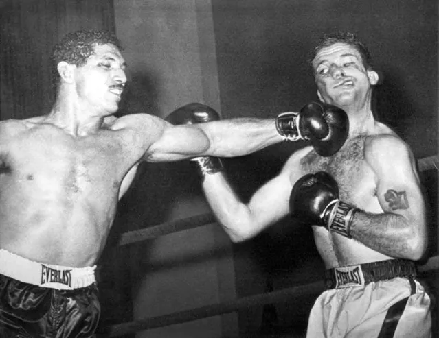 Cuban boxer Florentino Fernandez, left, swings a punch that contorts the face of his opponent, American Johnny Featherman, during their middleweight fight in Miami Beach, Florida, on December 30, 1965. The referee stopped the fight in the fifth round after Fernandez heavy blows opened deep cuts on Featherman's nose and eyes. It was the Cuban fighters 31st knockout in the 38 fights he has won. (Photo by AP Photo)