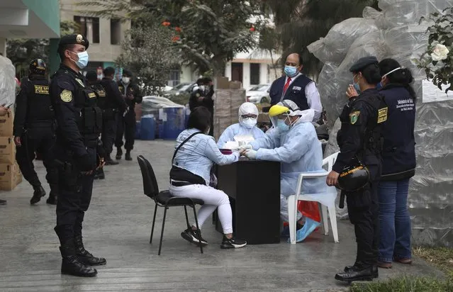 Police officers test a woman who was detained at a disco where thirteen people died during a stampede, for COVID-19 in Lima, Peru, Sunday, August 23, 2020. Officials said the stampede happened at a disco after a police raid to enforce the country's lockdown during the coronavirus pandemic. (Photo by Martin Mejia/AP Photo)