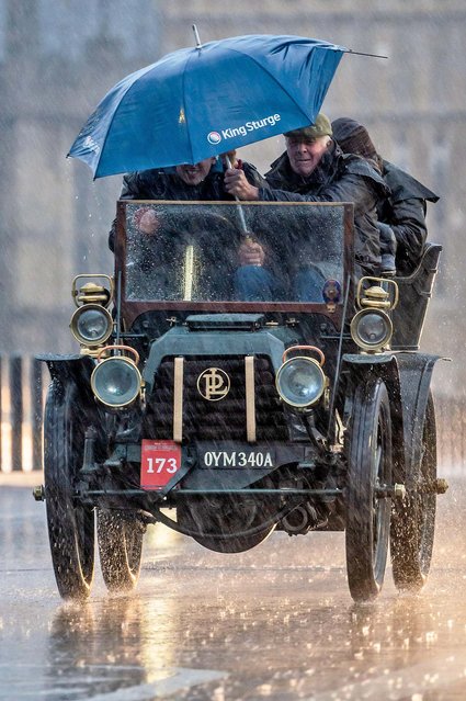 Participants shelter under an umbrella as they drive a 1903 Panhard et Levassor during the annual London to Brighton Veteran Car Run on November 6, 2022 over westminster bridge in heavy rain. (Photo by Guy Bell/Alamy Live News)