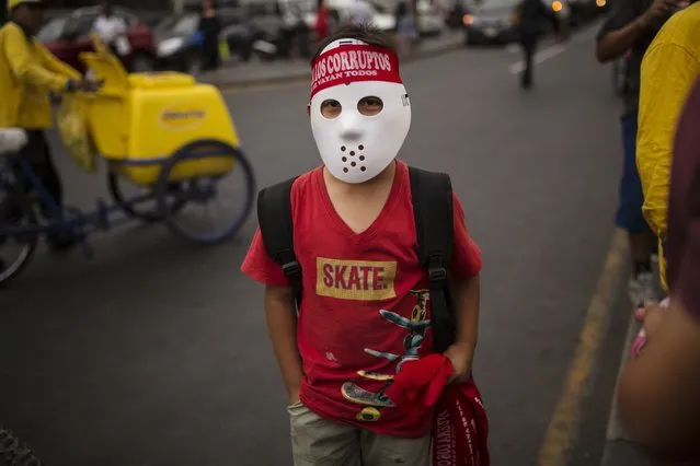 A boy wearing a mask sells headbands that read en Spanish “Let all the corrupt go”, during a protest the day after the resignation of Peru's President Pedro Pablo Kuczynski, in Lima, Peru, Thursday, March 22, 2018. Peru's congress is gearing up to consider whether or not to accept Kuczynski's resignation following the release of several videos appearing to show allies offering state contracts in exchange for votes against his pending impeachment. (Photo by Rodrigo Abd/AP Photo)