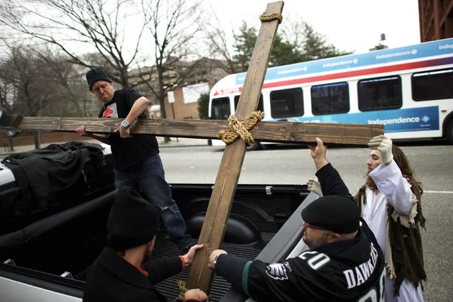 Supporters (L-R) Jason Krieck, 38, Ryan Bolli, 42, and Nando Fuselli, 38, assist Michael Grant, 28, “Philly Jesus”, in lashing the 12 foot cross to a truck following his 8 miles cross walk through North Philadelphia to Center City as part of a Christmas walk to spread the true message of the holiday in Philadelphia, Pennsylvania December 20, 2014. (Photo by Mark Makela/Reuters)