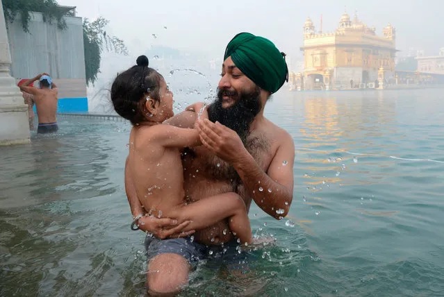 A Sikh devotee takes a dip in the holy sarovar (water tank) with a child on the occasion of New Year Day amid foggy conditions at the Golden Temple in Amritsar January 1, 2021. (Photo by Narinder Nanu/AFP Photo)