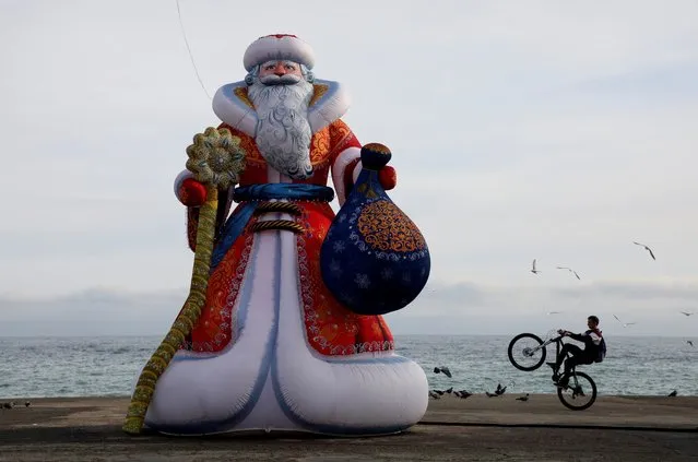 A bicyclist performs a trick on an embankment near an inflatable figure depicting Ded Moroz, the Russian equivalent of Santa Claus, ahead of the New Year and Christmas holiday season in the Black Sea resort of Alushta, Crimea on December 28, 2020. (Photo by Alexey Pavlishak/Reuters)
