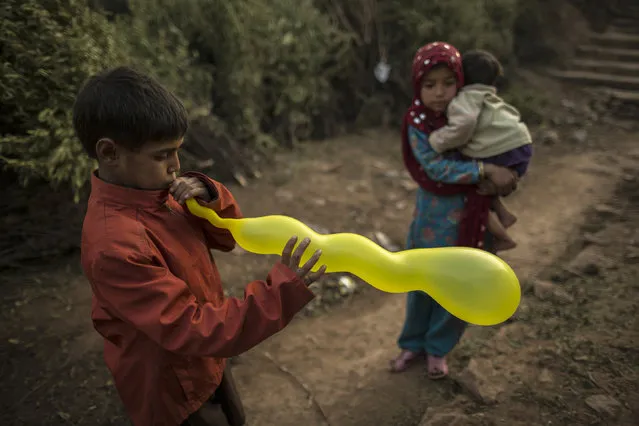 A boy inflates his balloon near a girl carrying her sibling at the entrance on the outskirts of Islamabad January 1, 2015. (Photo by Zohra Bensemra/Reuters)