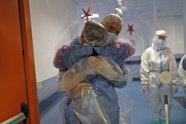 Ela Gubbiotti hugs her partner Giancarlo Vannimartini, an anesthesiologist who has been hospitalized for 10 days, in a safe room where patients and relatives can hug each other protected by a plastic film screen set up inside the COVID-19 ward of the Ospedale dei Castelli Hospital in Ariccia, near Rome, Wednesday, January 20, 2021. (Photo by Alessandra Tarantino/AP Photo)