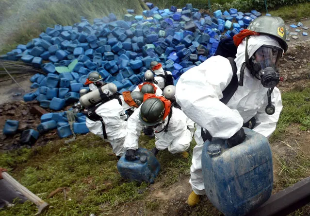 Firemen in protective gear clear barrels of hydrogen peroxide after a truck loaded with 18 tons of hydrogen peroxide overturned in Hangzhou, Zhejiang province, China August 25, 2006. (Photo by Reuters/China Daily)