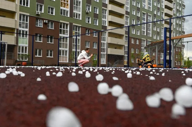 A woman takes photos of a child on a sports ground covered with hailstones following a hail storm in the Siberian city of Omsk, Russia on June 27, 2023. (Photo by Alexey Malgavko/Reuters)