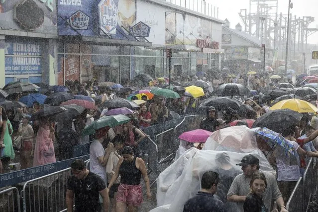 People take shelter from rain as the 2023 Nathan's Famous Fourth of July hot dog eating contest was paused in the Coney Island section of the Brooklyn borough of New York, Tuesday, July. 4, 2023. (Photo by Yuki Iwamura/AP Photo)