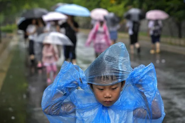 A child wearing a rain cover walks as visitors tour near the closed Forbidden City as a rainstorm soak Beijing, Sunday, July 30, 2023. Forbidden City and other tourist destinations in the capital city was ordered to close after authorities issued a red alert for rainstorms, as heavy rains brought by Typhoon Doksuri are expected to pound the Chinese capital and vast areas in the north. (Photo by Andy Wong/AP Photo)