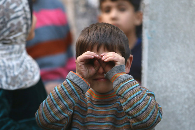 A boy reacts to a photographer while waiting to fill containers with water in a rebel-held besieged area of Aleppo, Syria December 10, 2016. (Photo by Abdalrhman Ismail/Reuters)