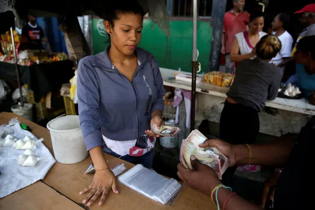 A vendor receives Venezuelan bolivar notes at her stall in a street market in the slum of Petare in Caracas, Venezuela, December 12, 2016. (Photo by Marco Bello/Reuters)