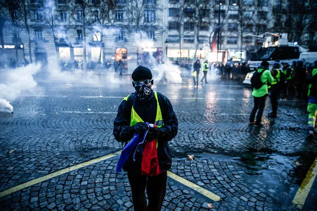 Protesters wearing yellow vests (gilets jaunes) stand amid smoke of tear gas during a demonstration against rising costs of living they blame on high taxes on the Champs-Elysees avenue in Paris, on December 15, 2018. The “Yellow Vests” (Gilets Jaunes) movement in France originally started as a protest about planned fuel hikes but has morphed into a mass protest against President's policies and top-down style of governing. (Photo by Abdul Abeissa/AFP Photo)
