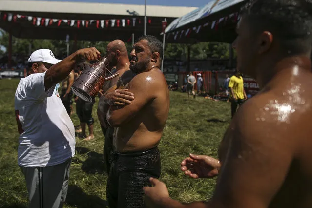 An “oiler”, someone charged with oiling up wrestlers and filling up oil pitchers, douses wrestlers in olive oil, during the 660th instalment of the annual Historic Kirkpinar Oil Wrestling championship, in Edirne, northwestern Turkey, Saturday, July 10, 2021.Thousands of Turkish wrestling fans flocked to the country's Greek border province to watch the championship of the sport that dates to the 14th century, after last year's contest was cancelled due to the coronavirus pandemic. The festival, one of the world's oldest wrestling events, was listed as an intangible cultural heritage event by UNESCO in 2010. (Photo by Emrah Gurel/AP Photo)