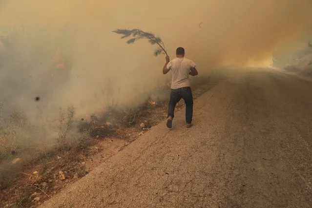 A man runs to extinguish a forest fire, at Qobayat village, in the northern Akkar province, Lebanon, Thursday, July 29, 2021. Lebanese firefighters are struggling for the second day to contain wildfires in the country's north that have spread across the border into Syria, civil defense officials in both countries said Thursday. (Photo by Hussein Malla/AP Photo)
