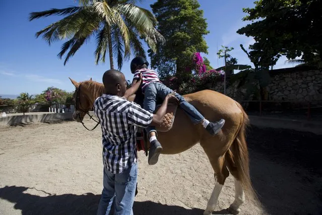 In this January 7, 2017 photo, Judeley Hans Debel dismounts Tic Tac with some help from his teacher at the Chateaublond Equestrian Center in Petion-Ville, Haiti. Advocates of therapeutic riding say it improves balance, coordination and confidence with the movements of the horse mimicking pelvic motions involved in human walking. (Photo by Dieu Nalio Chery/AP Photo)