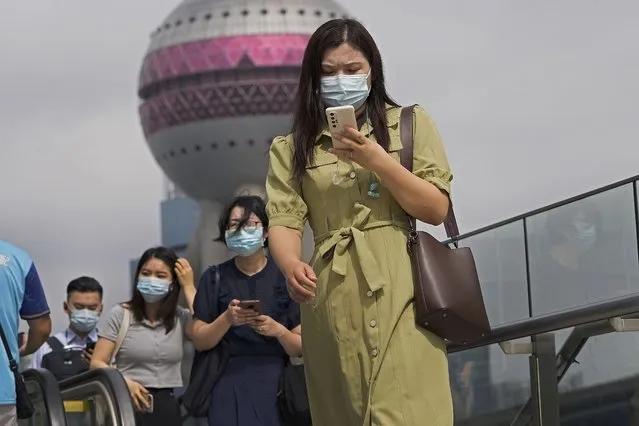 People wearing face masks to help protect from coronavirus using their smartphones walk on a pedestrian overhead bridge in front of the Oriental Pearl TV Tower at the Pudong Financial District in Shanghai, China, on August 25, 2021. Chinese regulators will exercise greater control over the algorithms used by Chinese technology firms to personalize and recommend content, in the latest move in a regulation spree across the internet sector. (Photo by Andy Wong/AP Photo)
