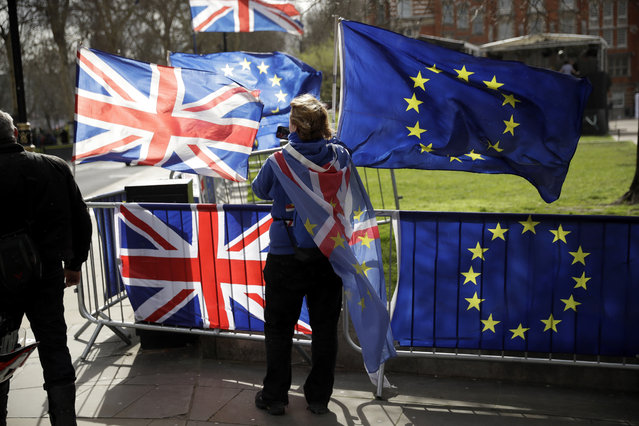 An anti-Brexit supporter stands by European and British Union flags placed opposite the Houses of Parliament in London, Monday, March 18, 2019. British Prime Minister Theresa May was making a last-minute push Monday to win support for her European Union divorce deal, warning opponents that failure to approve it would mean a long – and possibly indefinite – delay to Brexit. Parliament has rejected the agreement twice, but May aims to try a third time this week if she can persuade enough lawmakers to change their minds. (Photo by Matt Dunham/AP Photo)
