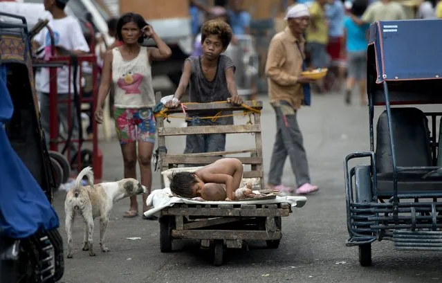 A boy pushes a wooden cart with his siblings on it at a market in Manila on April 24, 2015. (Photo by Noel Celis/AFP Photo)